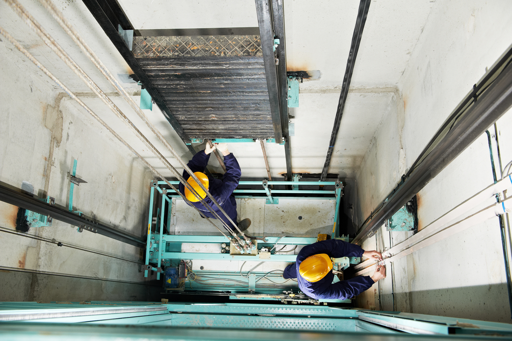 two machinist worker technicians at work adjusting lift with spanners in elevator hoistway