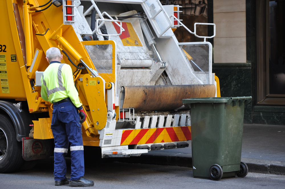 A garbage truck driver working - emptying rubbish into his truck.